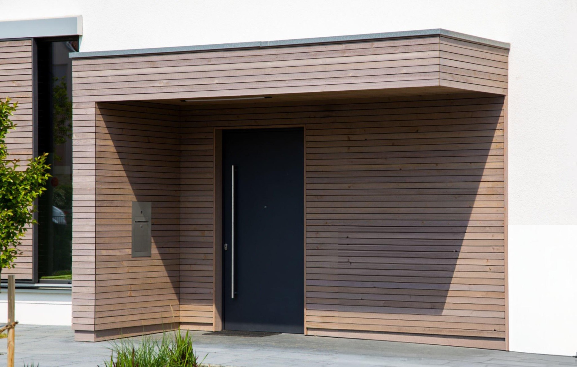 verputztes Haus mit Holz-Fassadenverkleidung im Eingangsbereich